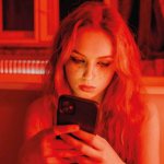 Girl in red lighting looks at the phone and cries